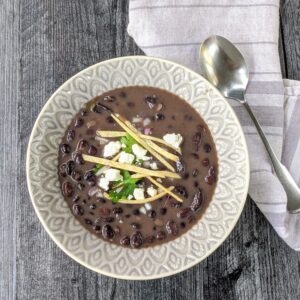 bowl of instant pot black bean soup garnished with sour cream, cilantro and tortilla strips with spoon