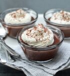 three ramekins with chocolate pudding topped with whipped cream and chocolate shavings.