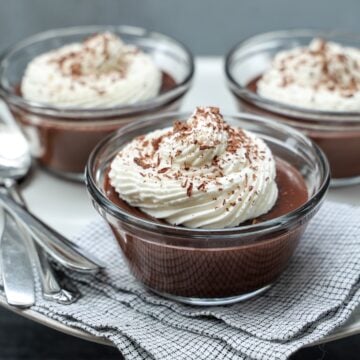 three ramekins with chocolate pudding topped with whipped cream and chocolate shavings.