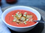 Bowl of gazpacho topped with croutons, chopped cucumber and parsley