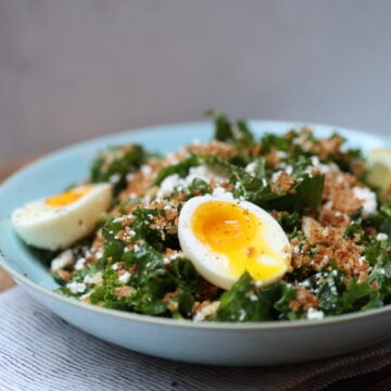 bowl of kale salad with toasted garlicky crumbs, crumbled feat, and 2 halves of a sift-boiled egg