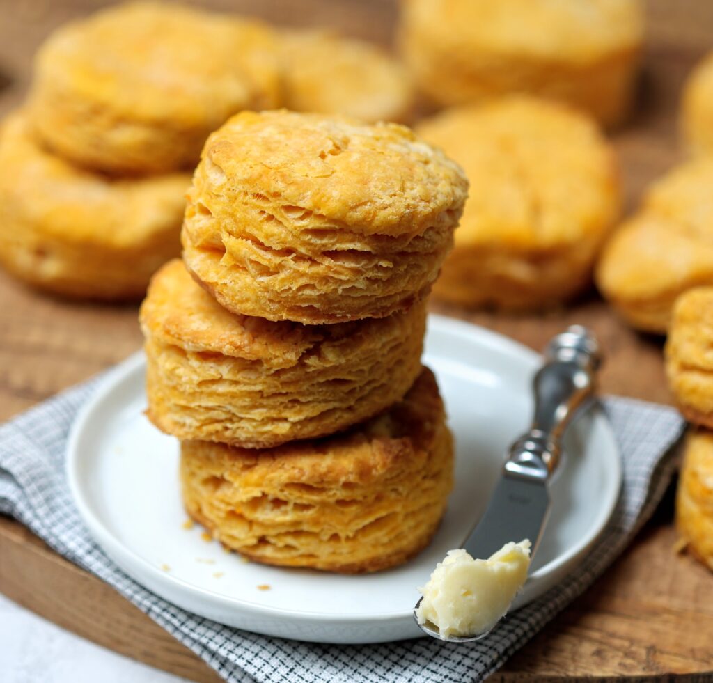 Stack of biscuits on a white plate. A butter knife with a dollop of cinnamon butter sits next to the biscuits