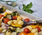 gnocchi with vegetables and pesto on a sheet pan with a serving spoon