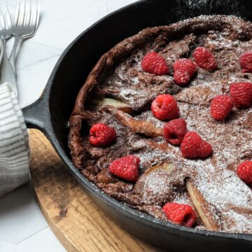 cast-iron skillet with chocolate Dutch baby with fresh raspberries and powdered sugar