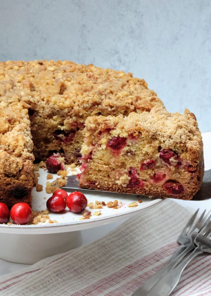 Cake stand with cranberry streusel coffee cake that has a slice being pulled from it