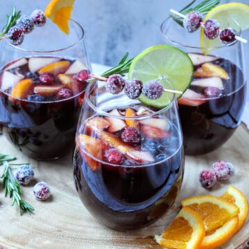 three glasses of Holiday Red Wine Sangria with fresh fruit, sugared cranberries and sprig of rosemary garnish.