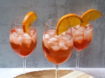 stemmed wine glasses with aperol spritz, ice, and orange garnish