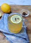 glass mug with hot toddy garnished with lemon slice and whole cloves.