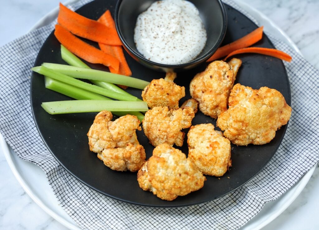 A plate of crispy buffalo cauliflower bites served with ranch dressing and carrot and celery sticks