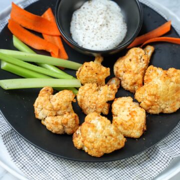 plate with cauliflower bites, bowl of ranch dressing and carrot and celery sticks.