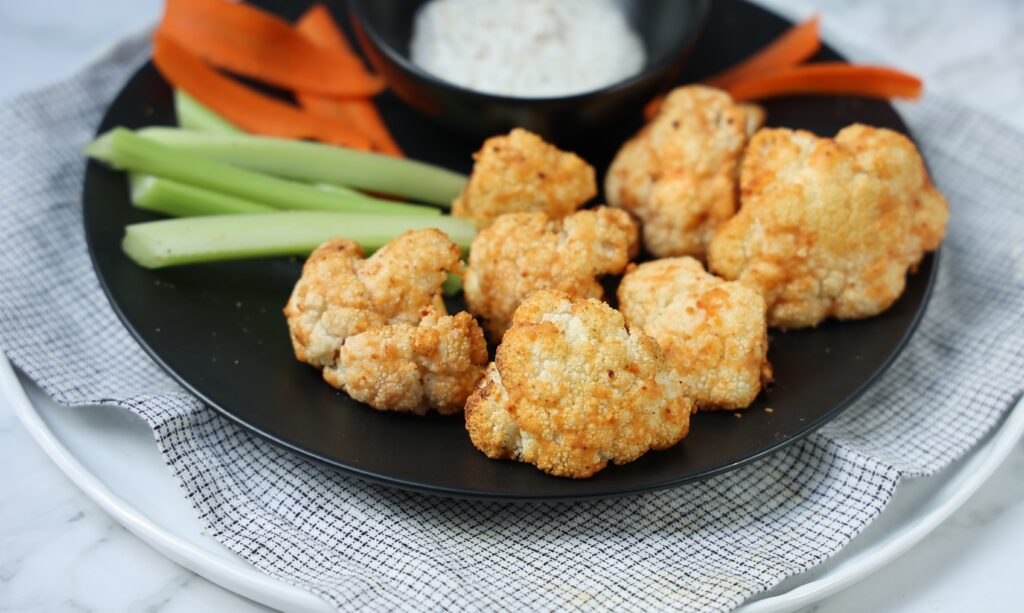 Prepared and plated cauliflower bites with side of dipping sauce and carrots and celery sticks