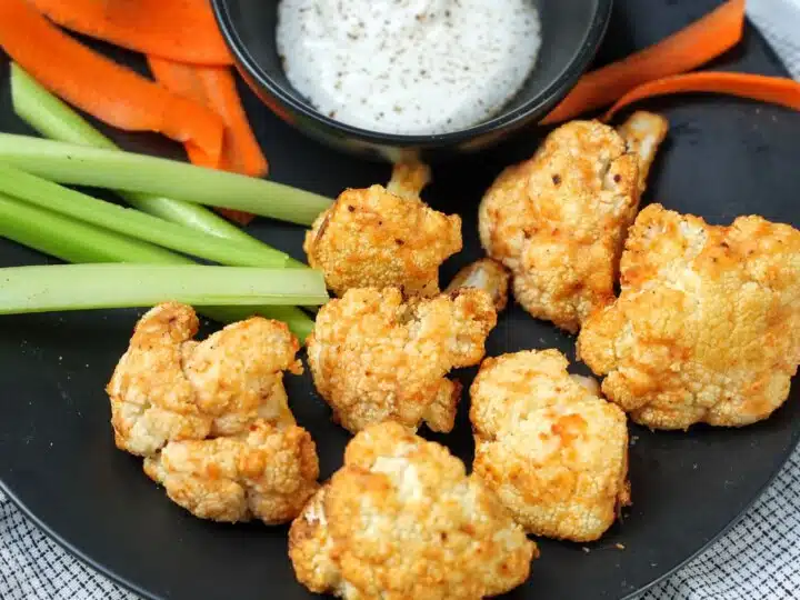 Plate with crispy cauliflower bites with blue cheese dip, carrots and celery sticks.