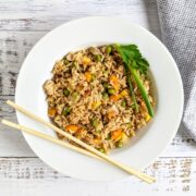 chicken fried rice in a white bowl with chopsticks on the edge