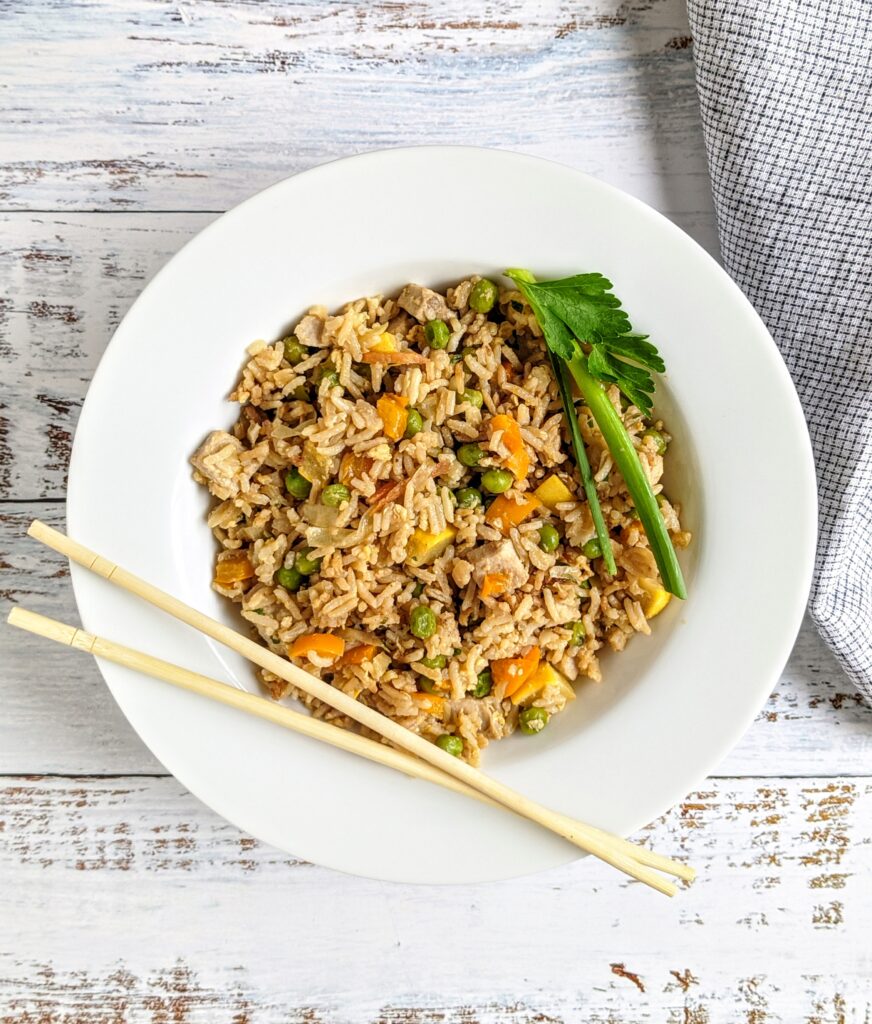 chicken fried rice in a white bowl with chopsticks on the edge