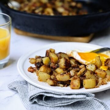 Plate of skillet potates with fried egg and skillet with potatoes in background.