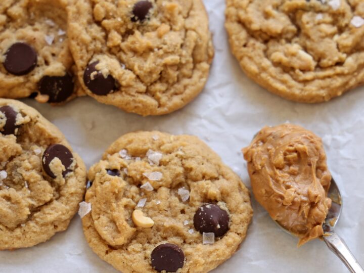 Soft peanut butter dark chocolate chip cookies with flay sea salt on baking sheet.