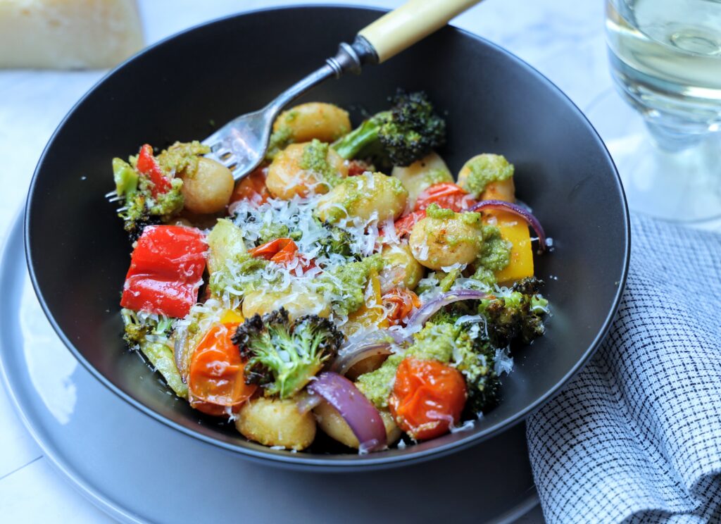 Bowl of roasted gnocchi and vegetables in pesto sauce, garnished with parmesan cheese