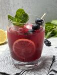 Glass with blueberry ginger lemonade garnished with fresh mint, lemon slice, and berries.