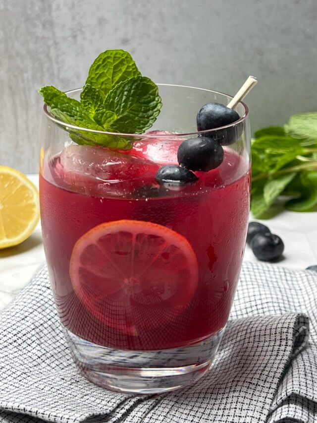 Glass of blueberry ginger lemonade. Garnished with blueberries, lemon slice, and mint