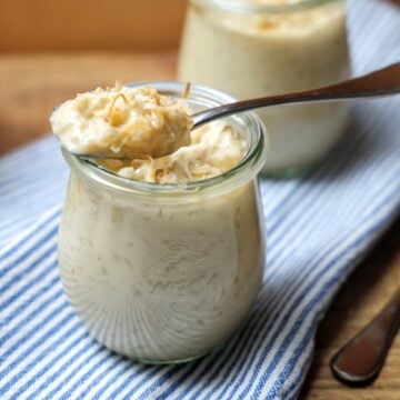 Serving of rice pudding in a glass dish, topped with shredded coconut. A spoon is dipping into the dish