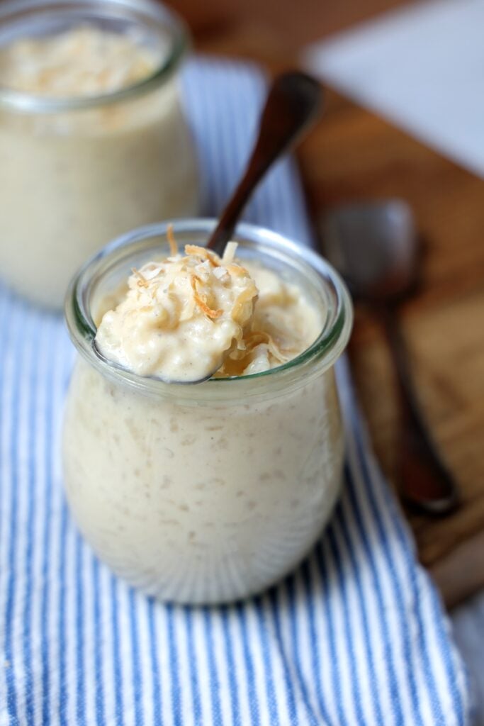 Coconut rice pudding in a glass dish topped with shredded coconut and a spoon dipping into the dish