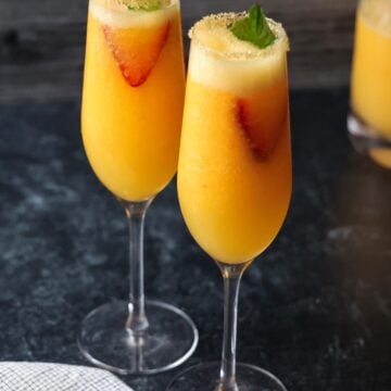 Two sugar-rimmed champagne flutes filled with peach bellini.