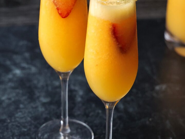 Two sugar-rimmed champagne flutes filled with peach bellini.