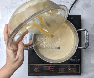 Sauce pan of milk and rice mixture. A bowl of beaten egg yolks, sugar, vanilla, and cardamom is being added to the sauce pan