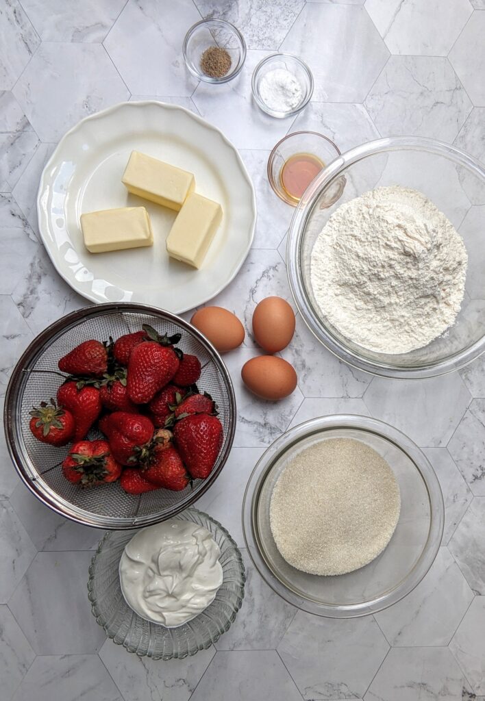 Overhead shot of ingredients: flour, butter, sugar, strawberries, eggs, sour cream, vanilla, baking powder and soda, and cardamom