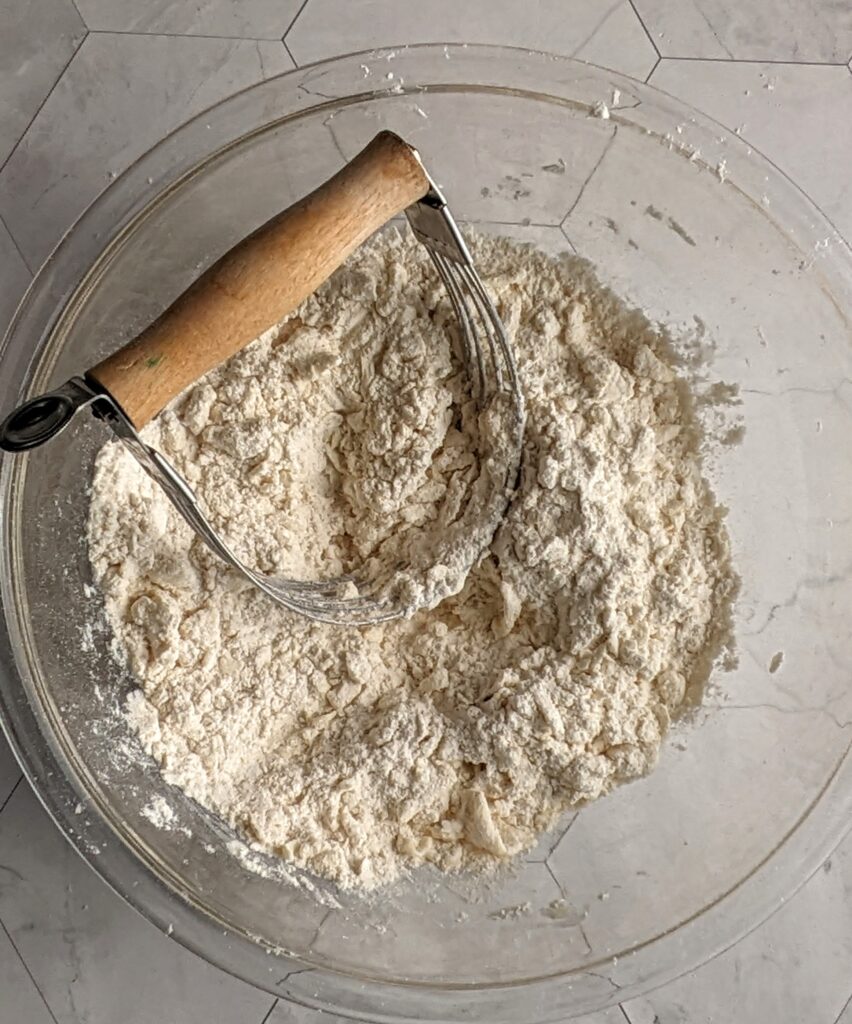 glass bowl of flour, cold butter, oats, orange zest, cinnamon, salt, baking soda, and baking powder.