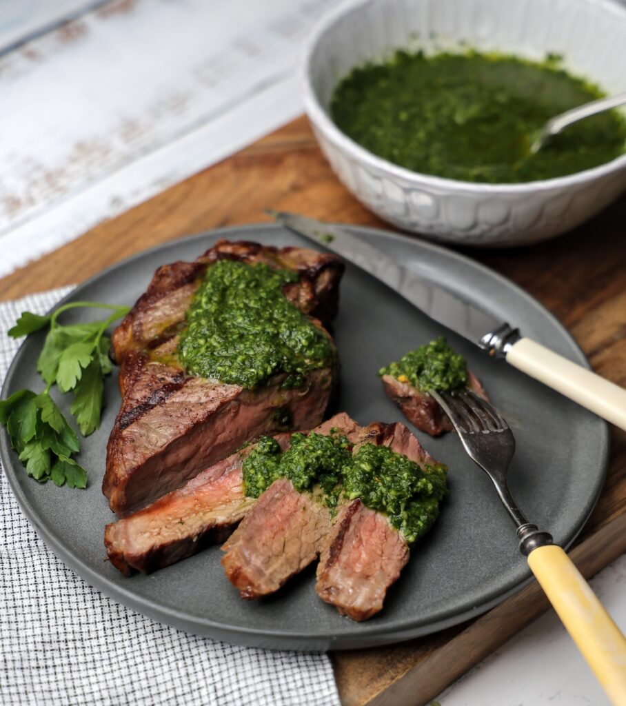 Plate the steak slices topped woth chimichurri sauce. Bowl of chimichurri sauce in the background.