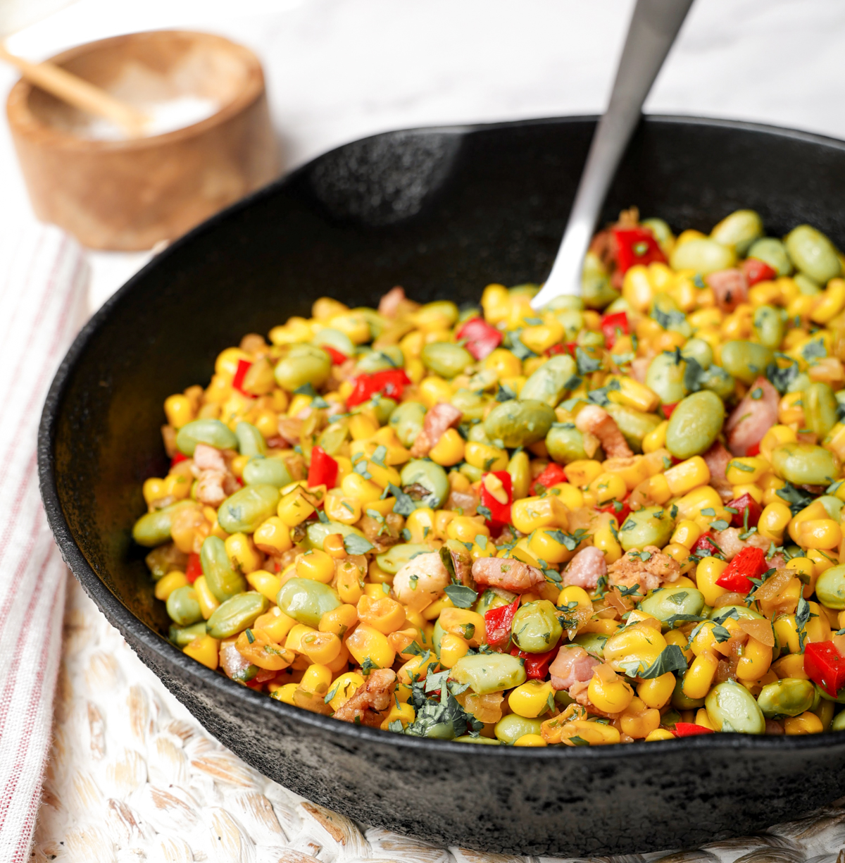 Cast iron skillet with succotash and large spoon in it. 