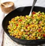 Cast iron skillet with edamame succotash and spoon.