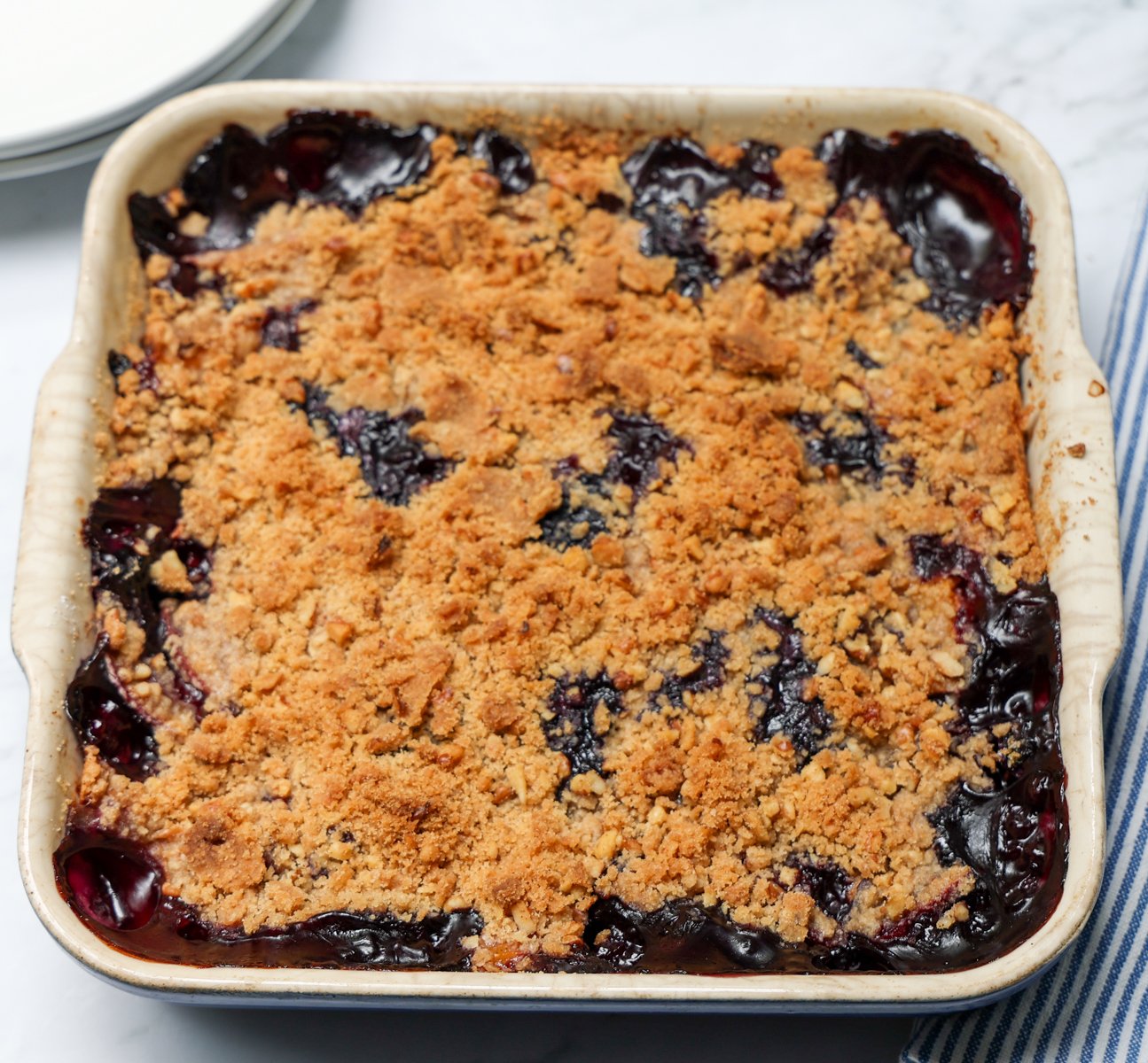 overhead view of baked peach blueberry crisp in square ceramic baking dish.