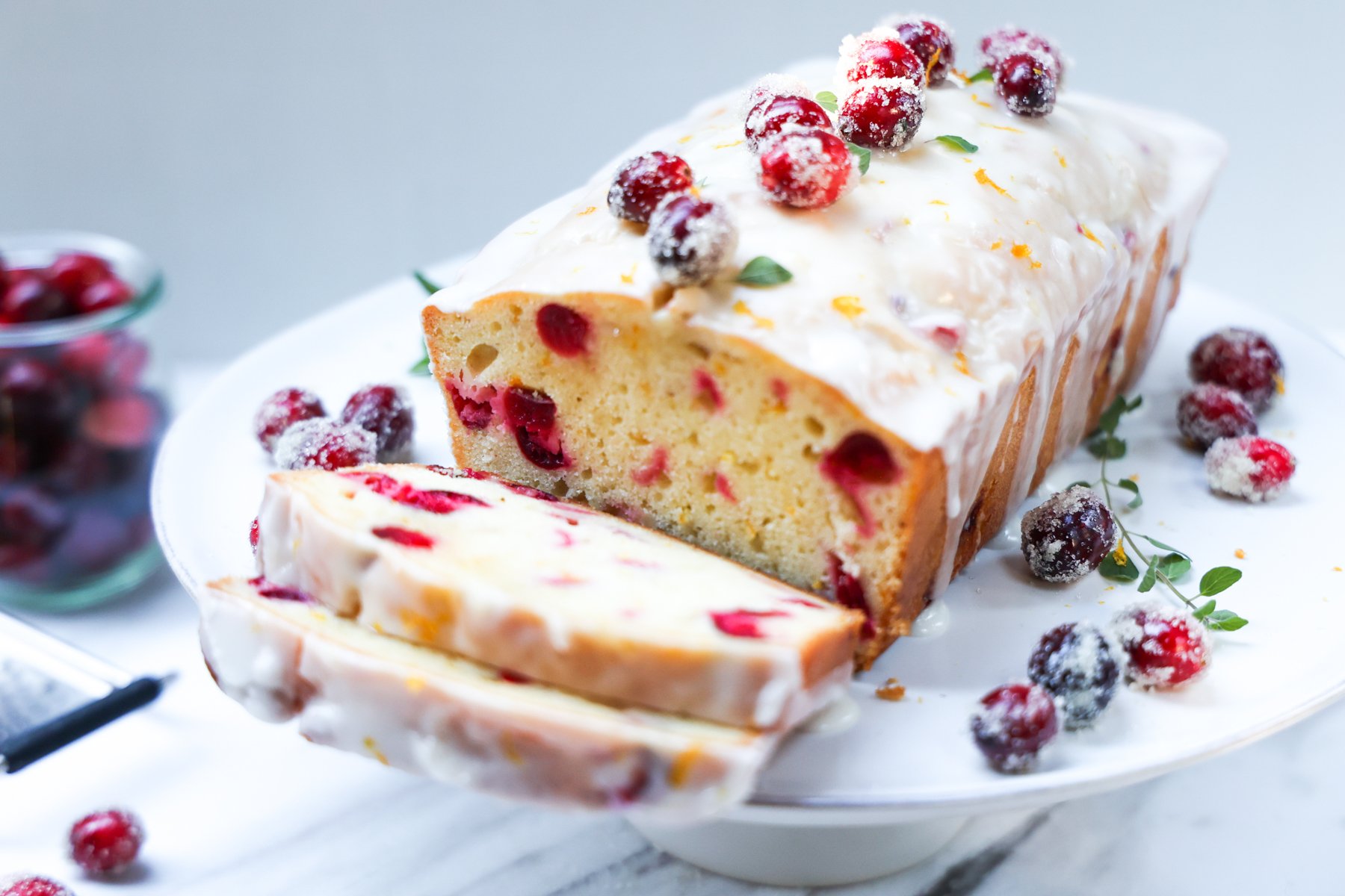 Cranberry Orange loaf cake on cake stand with 2 slices  and decorated with sugared cranberries.
