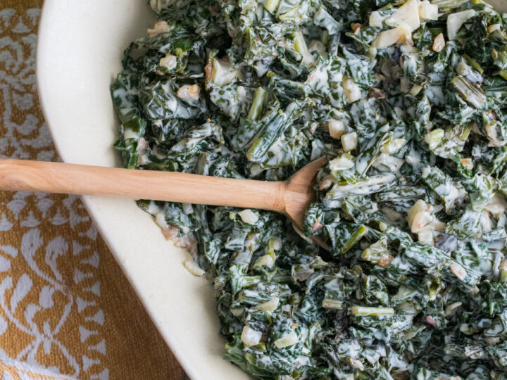 Overhead close up of creamed kale in bowl with serving spoon.