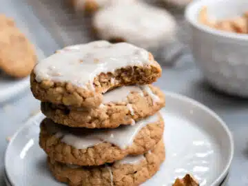 Stack of 4 iced oatmeal cookies on a white plate, with bite out of the top one.
