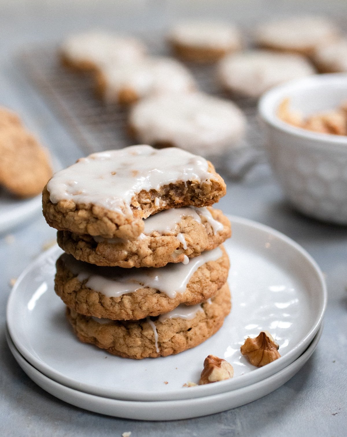 Stack of 4 iced oatmeal cookies on white plate with bite out of one on top.