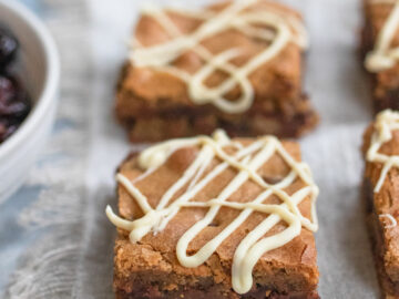 Close up of two squares of Chocolate Chip Blondies with a. white chocolate drizzle on top.