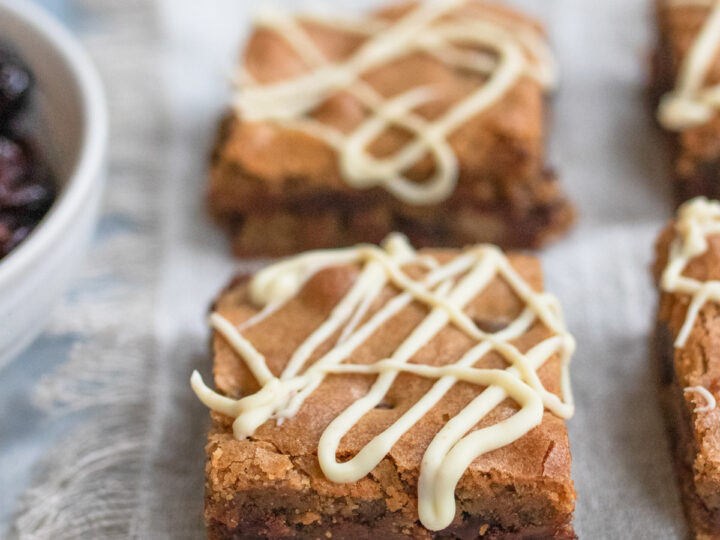Close up of two squares of Chocolate Chip Blondies with a. white chocolate drizzle on top.