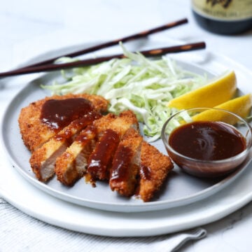 Plate with pork katsu sliced with a small bowl of sauce and shredded cabbage.