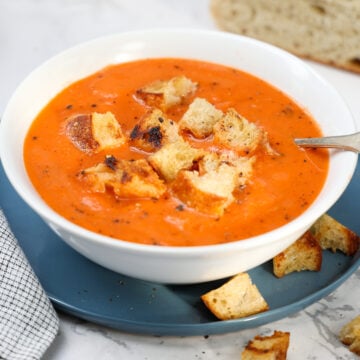 White bowl of tomato soup topped with croutons.