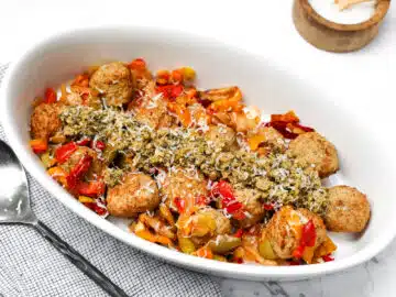 white oval dish with meatballs, vegetables and pesto.