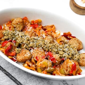 white oval dish with meatballs, vegetables and pesto.