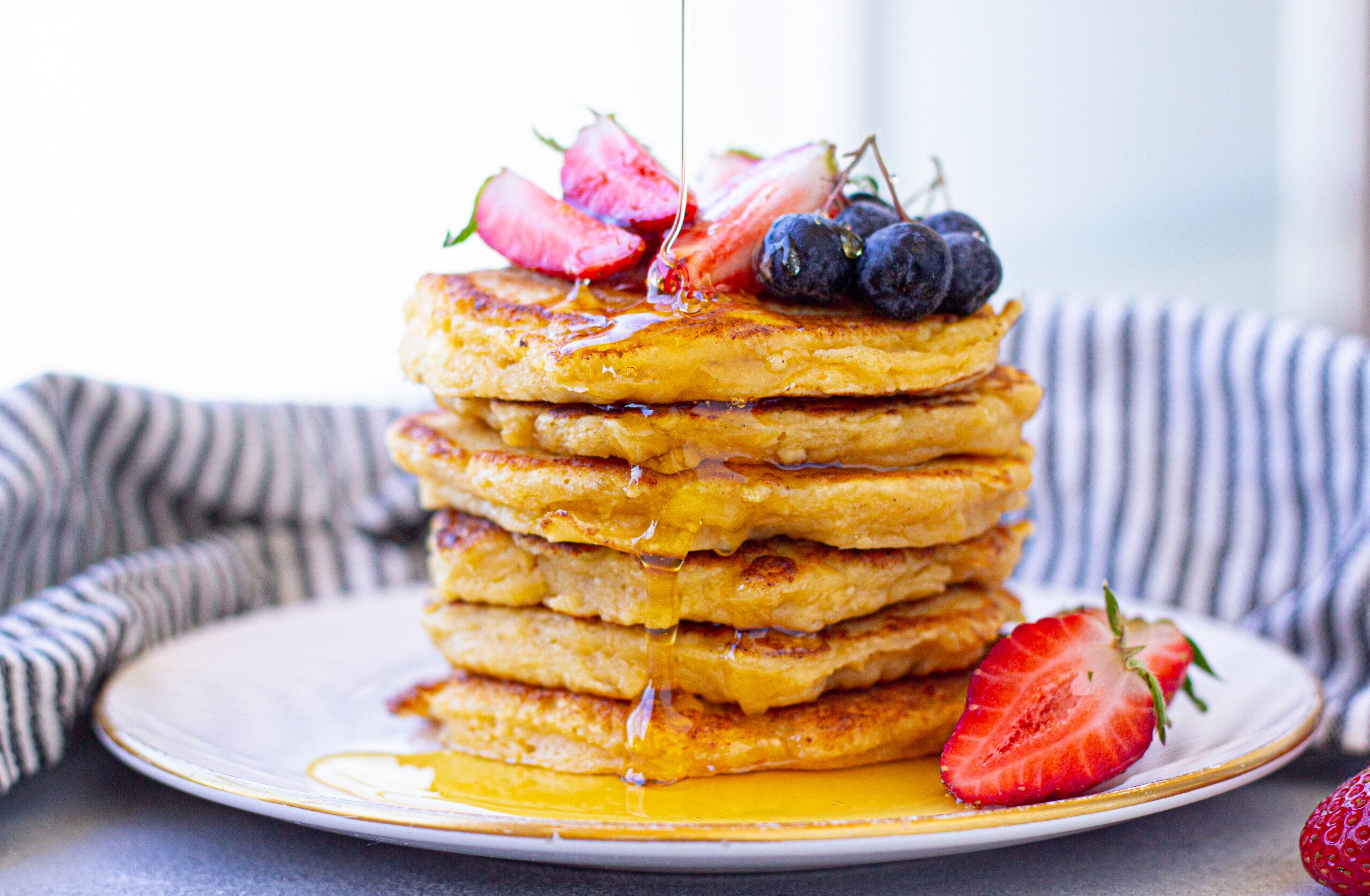 Stack of cottage cheese pancakes with fruit on top and maple syrup.