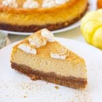 Slice of pumpkin pie cheesecake on plate with whole cheesecake in background.