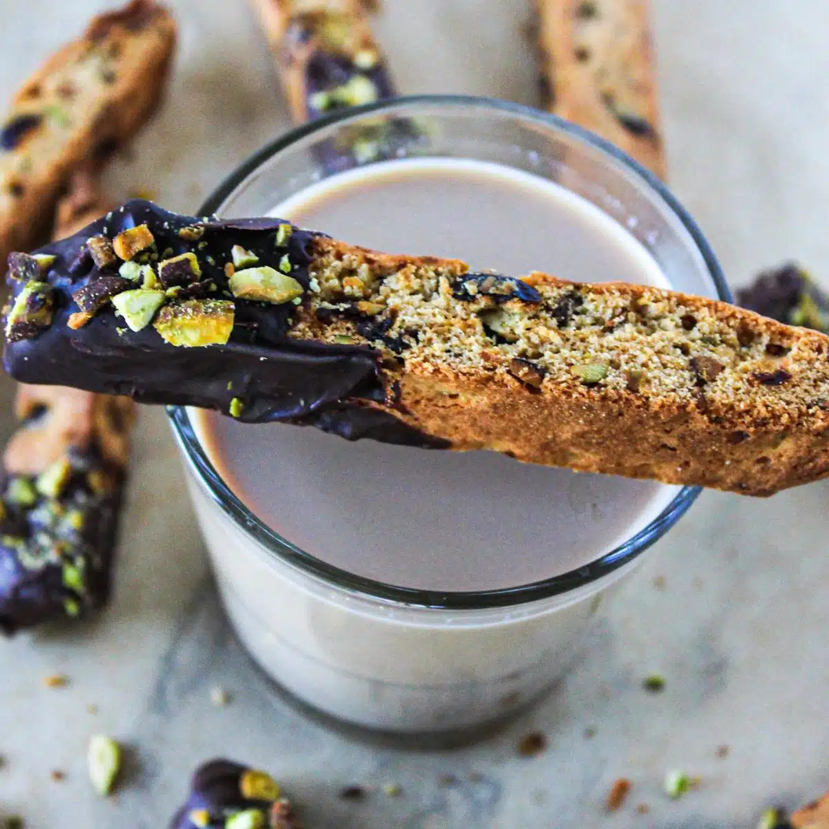 Chocolate-Dipped Cherry and Pistachio Biscotti sitting over a glass of milk. 