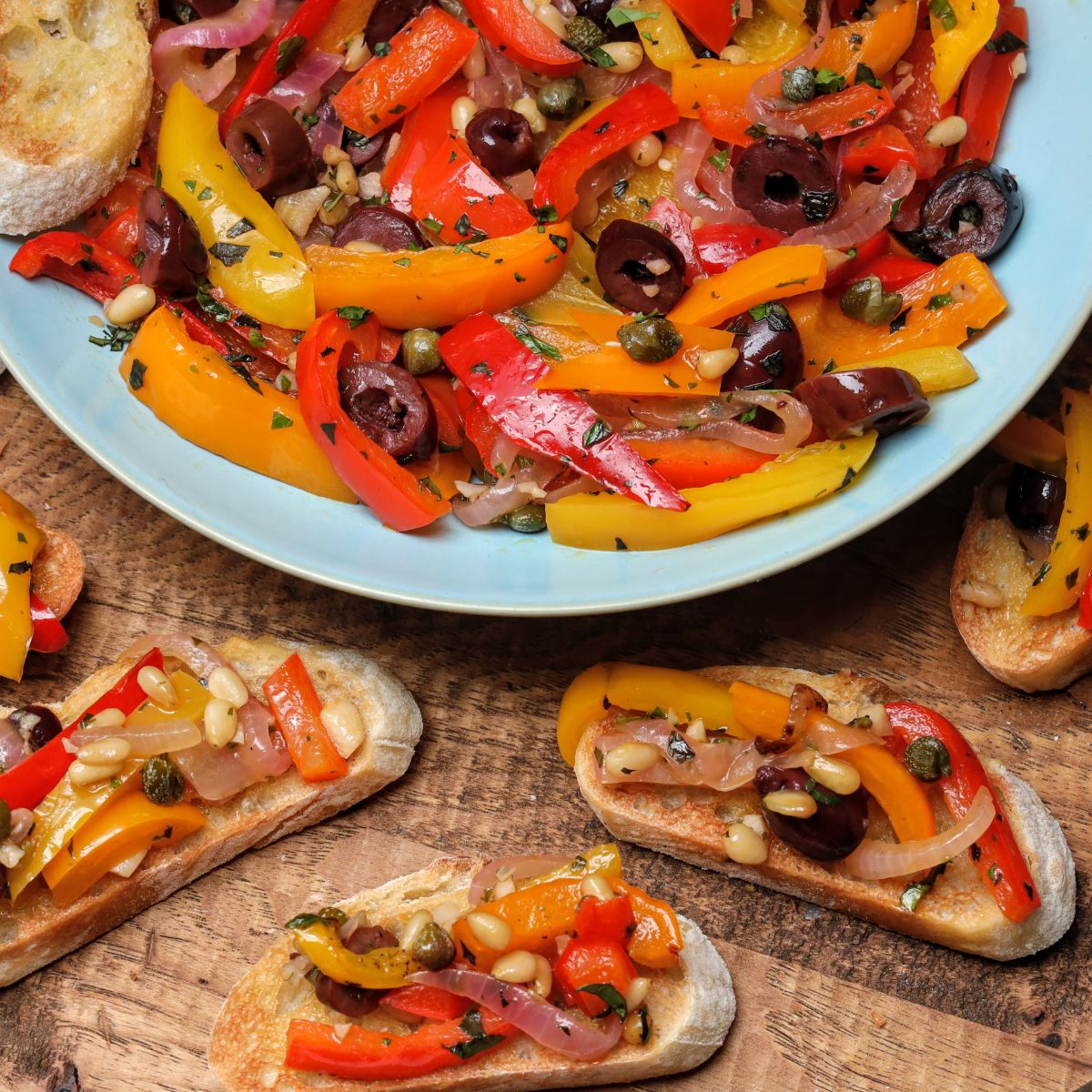 This is a close-up shot of peperonata in a blue serving bowl and spread on baguette slices.