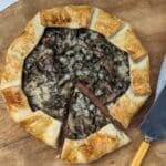 Mushroom tart on board with slice cut.