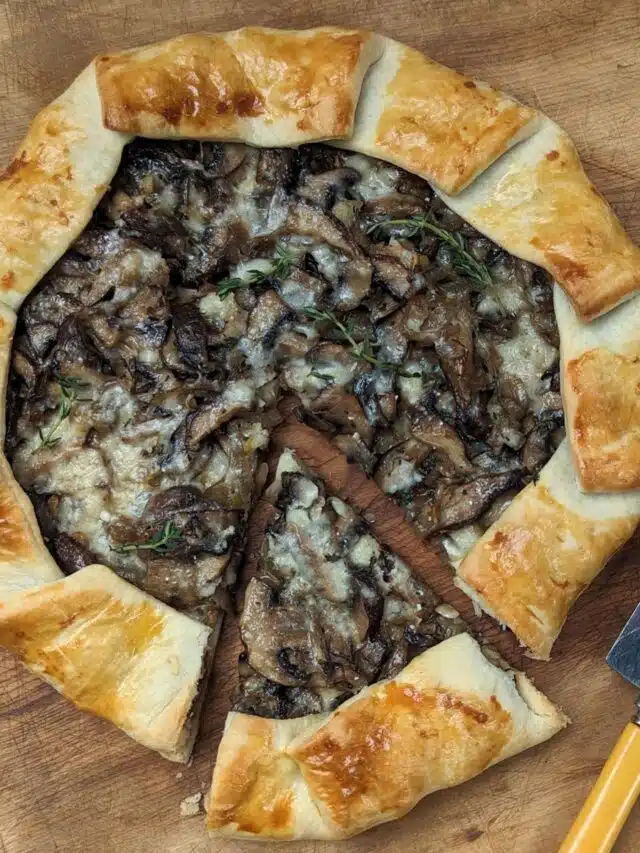 Mushroom tart on board with slice cut.